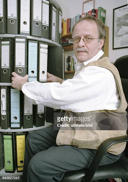 Der Journalist Hans Leyendecker in seinem Arbeitszimmer. Er sitzt auf einem Bürostuhl vor einem runden, drehbaren Regal mit Aktenordnern. .