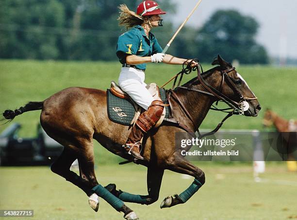 Eine Polospielerin auf dem Rücken ihres Pferdes im Galopp. Die Spielerin trägt einen Helm mit Gesichtsschutz und Bandagen aus Leder am Bein. In der...