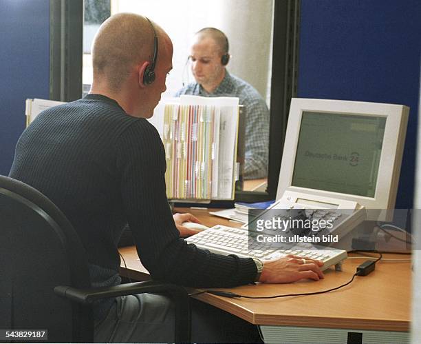 Ein Call Center Agent sitzt an seinem Computerarbeitsplatz in einem Call Center der Bank 24. Der Mann hat ein Headset auf und bedient Tastatur und...