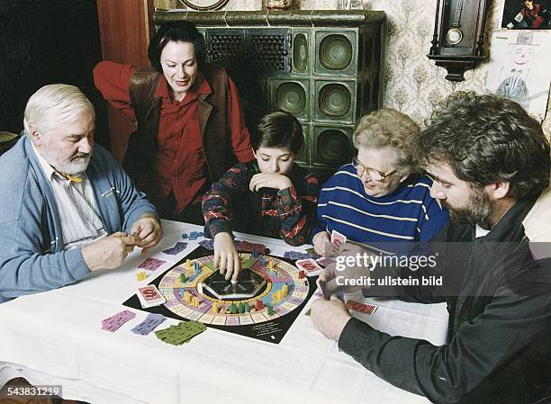 Eine Familie, bestehend aus Großvater, Mutter, Kind, Großmutter und Vater, hat sich in einem altdeutsch eingerichteten Wohnzimmer um einen Tisch...