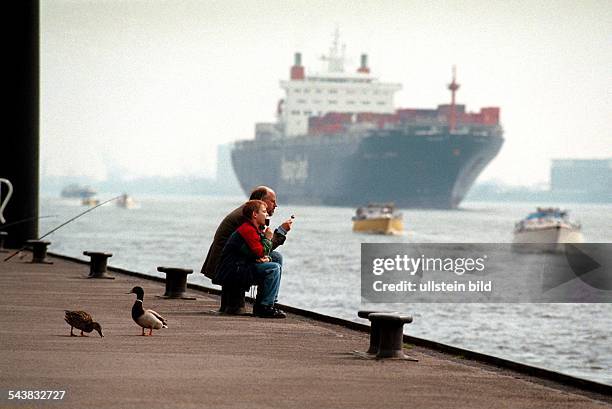 Familienidylle auf dem Anleger Op''n Bulln in Blankenese. Auf einem der Poller sitzt ein Vater mit seinem Sohn in der Sonne. Beide essen ein Eis am...