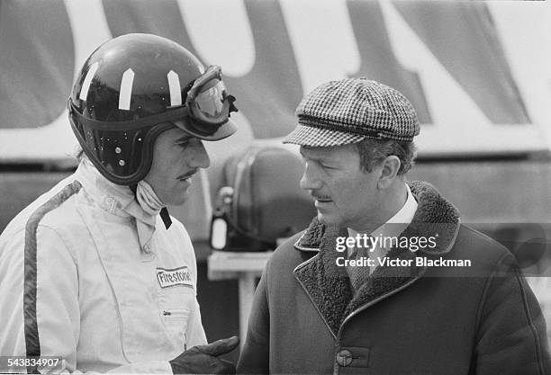 English inventor, engineer, and founder of Lotus Cars Colin Chapman with British racing driver Graham Hill taking a break from practice sessions at...