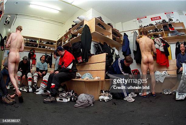 Die Spieler der Eishockey-Mannschaft "Hannover Scorpions" in der Umkleidekabine. Einige Eishockeyspieler sitzen im Sportdress auf Bänken, umgeben von...
