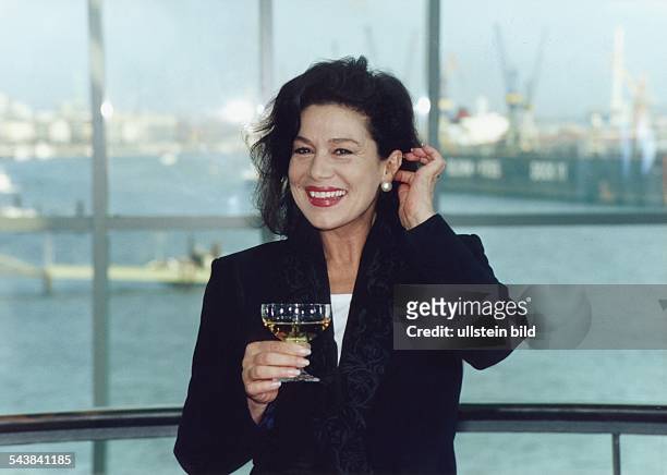 Schauspielerin Hannelore Elsner mit Glas in der Hand vor einer Fensterfront. Im Hintergrund ist der Hamburger Hafen zu sehen. Aufgenommen April 1993.
