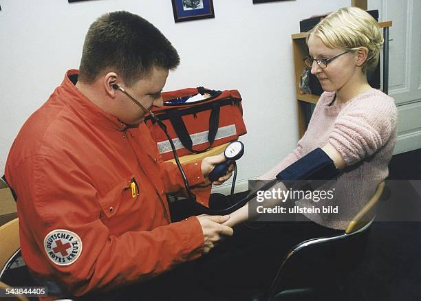 Ein Mitarbeiter des Deutschen Roten Kreuzes misst mit einem Blutdruckmessgerät bei einer jungen Frau den Blutdruck. Aufgenommen 1999.