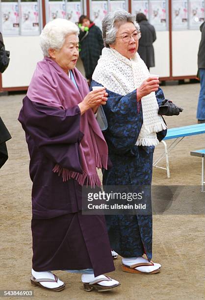 Zwei alte Frauen im Stadtpark von Tokio. Sie halten Pappbecher in ihren Händen und tragen Wollschals über ihren Kimonos. .