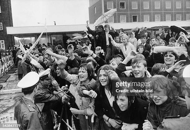 Hunderte nass geregneter Fans warten winkend und jubelnd auf ihre Idole, die englische Popgruppe "The Beatles". Die tobende Menschenmenge wird von...