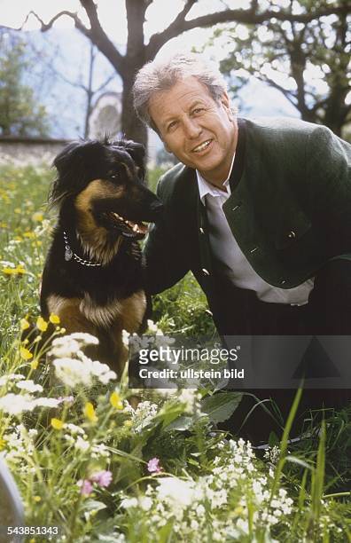 Der "Bergdoktor" Gerhard Lippert aus der gleichnamigen TV-Serie kniet neben seinem Schäferhund in einer bunten Blumenwiese. Undatiertes Foto.