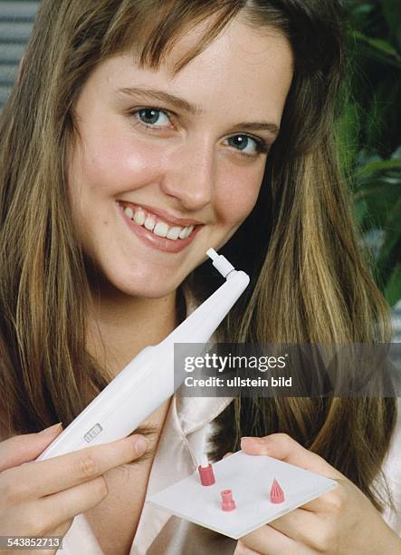 Eine junge Frau hält einen Plaque-Entferner und die dazugehörenden Aufsätze in ihrer Hand. Das Gerät beseitigt Zahnstein und Zahnbeläge, poliert die...