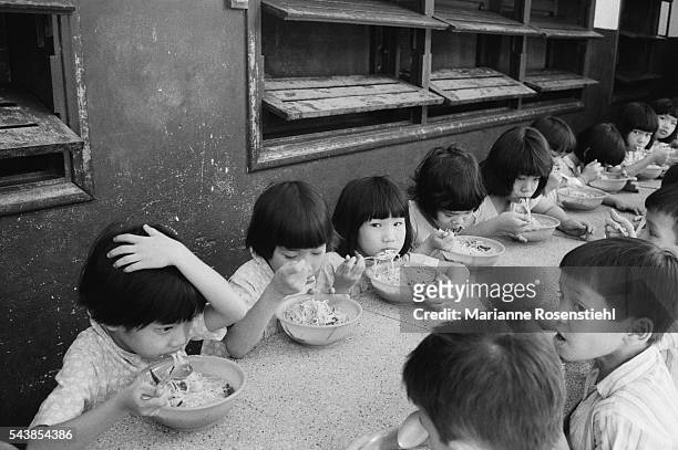 Lunchtime in the orphanage, where the young girls are seated on one side of the table and the boys are seated opposite.