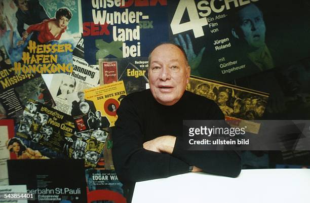 Der Hamburger Regisseur Jürgen Roland steht vor einer Wand mit Filmplakaten, in denen er Regie geführt hat. .