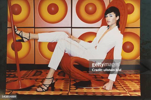 Das 15-jährige deutsche Fotomodell Teresa Lourenco sitzt in einem weißen Hosenanzug in einem orangefarbenen Sessel. Einen Fuß hat sie an einen roten...