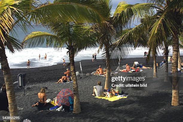 La Palma .Die weiße Gischt der auslaufenden Brandungswellen perlt über den schwarzen Sandstrand von Naos, wo Touristen auf dem schwarzen Lavasand...