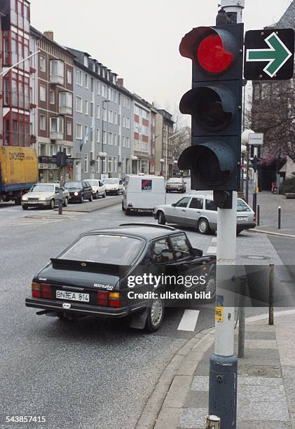 Neben einer auf rot geschalteten Ampel weist ein grüner Pfeil daraufhin, dass Autofahrern das Abbiegen dennoch erlaubt ist. Auto, Verkehrsteilnehmer,...