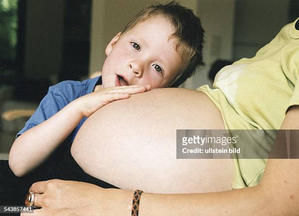 Ein Junge legt seinen Kopf und seine Hand auf den Bauch seiner schwangeren Mutter. Kind; Nachwuchs; Bruder; Erstgeborener. .