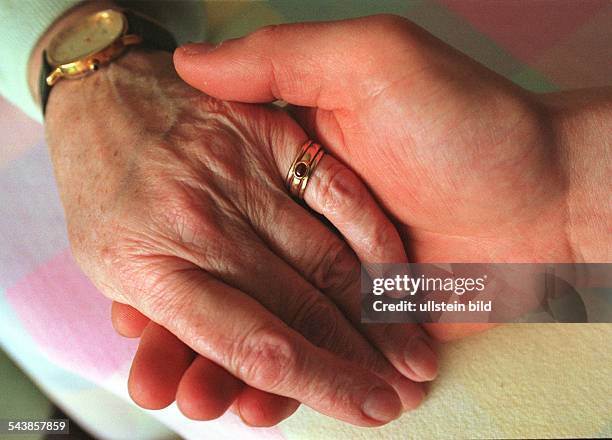 Eine Hand hält die Hand einer alten Frau. Die Seniorin trägt Goldringe am dem kleinen Finger und eine Armbanduhr. Alter; Rente; Betreuung; Trost;...