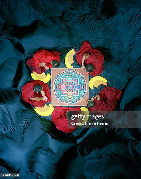 Buddhist monks gather round a mandala composed of grains of colored sand. A mandala, a symbol of impermanence, is dispersed after its construction,...