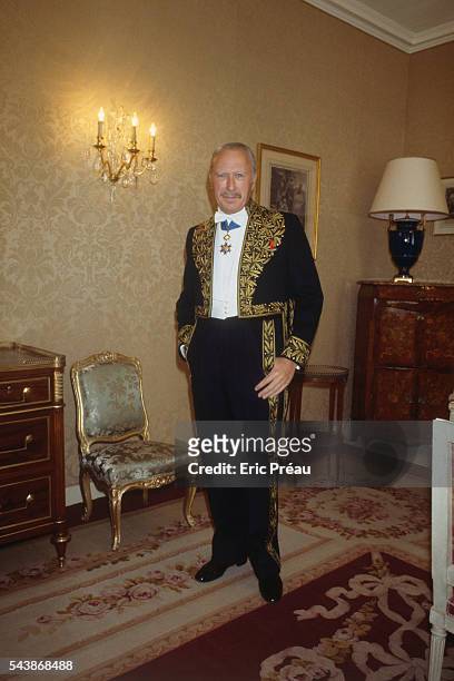 French novelist and lampoonist Jean Dutourd standing in his home, dressed in the gold silk-embroidered suit of an academic. He was elected to the...