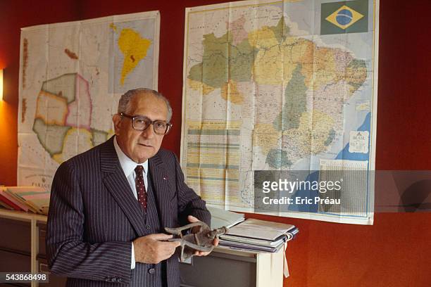 French Americanist, ethnologist, politician and essayist Jacques Soustelle standing in front of maps of southern Brazil and Paraguay in his home. On...