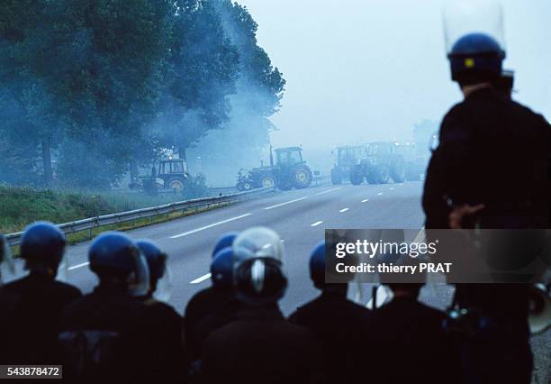 Agricultural workers from the "Coordination Rurale Union Nationale" block access to the Paris region during demonstrations as riot police look on.