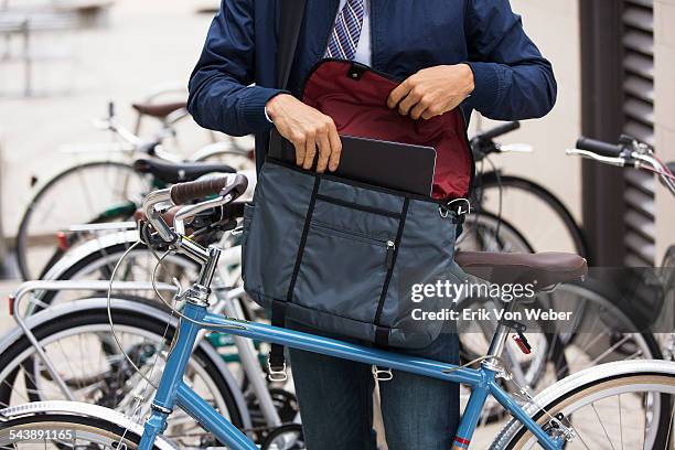 man with bicycle putting laptop into courier bag - borsa messenger foto e immagini stock