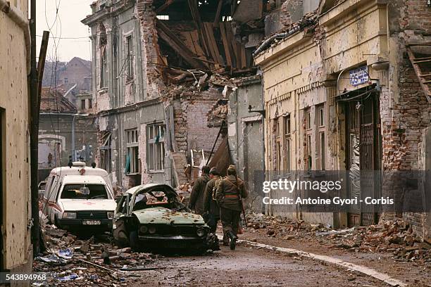 Yugoslavian soldiers and Serb paramilitaries, including Zeljko "Arkan" Raznatovic, walk past bombed buildings riddled with bullet holes and streets...