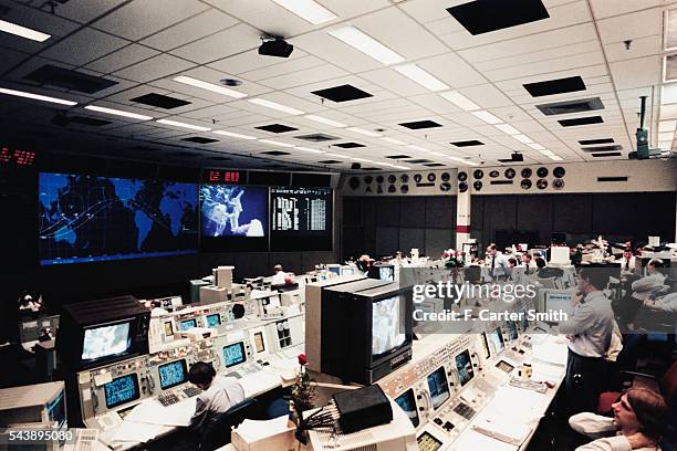 Flight controllers in the control room monitor two space walkers on television during the STS-61 Mission.