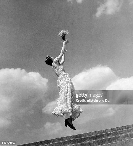 Woman waering a summer dress jumps and throws a bouquet of flowers in the air - ca. 1936- Photographer: Regine Relang- Published by: 'Die Dame'...