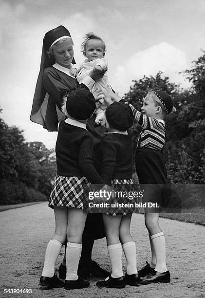 Sister wearing a baby on her arms, encircled by children: two girls wearing small tartan skirt and berets and a boy in a striped pullover - ca. 1935-...