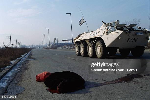 Corpse of a woman lies in the road next to a United Nations medical vehicle. The woman was a victim of the siege of Sarajevo during the Yugoslavian...