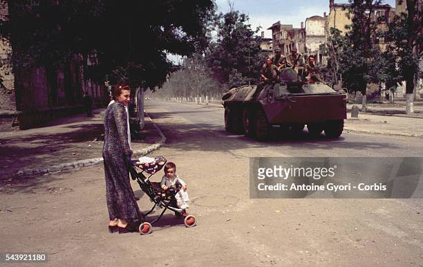 Chechen woman walks her child in the streets of Grozny as Russian soldiers look on.