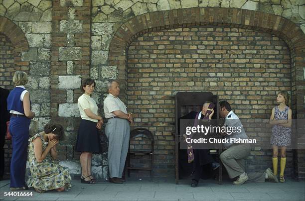 At the Jasna Gora monastery, an unidentified clergyman takes confession from people on either side of his portable confessional stall, Czestochowa,...