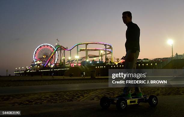 Man rides his electric skateboard past a lit up Santa Monica pier in Santa Monica, California on June 30 as a Summer night falls on the last day of...