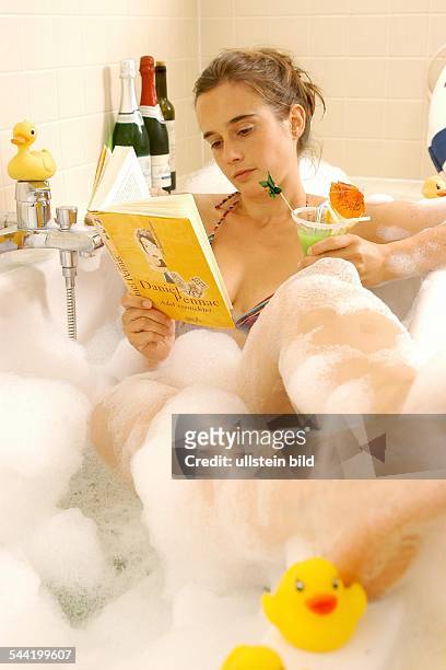 Deutschland, Junge Frau entspannt sich in der Badewanne mit einem Buch und einem Cocktail,- -vorhanden