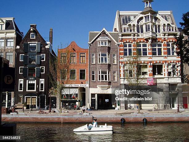 Niederlande, Amsterdam: Touristen fahren mit einem Tretboot auf einer Gracht an schoenen alten Haeusern vorbei.