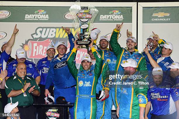 Aric Almirola, driver of the Fresh From Florida Ford, raises the winner's trophy in Victory Lane after taking the checkered flag in the NASCAR...