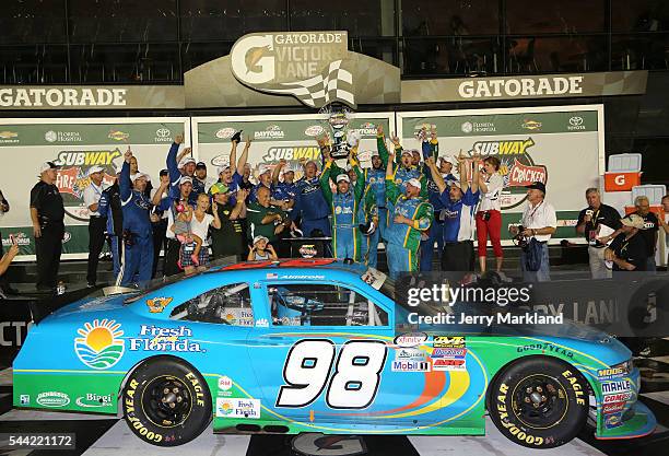 Aric Almirola, driver of the Fresh From Florida Ford, raises the winner's trophy in Victory Lane after taking the checkered flag in the NASCAR...