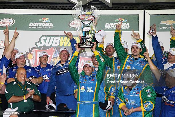 Aric Almirola, driver of the Fresh From Florida Ford, raises the winner's trophy in Victory Lane after taking the checkered flag in the NASCAR...