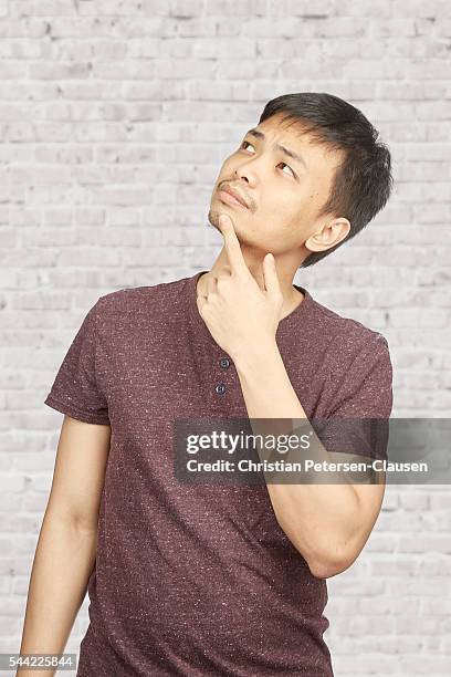 young asian man thinking looking up - hand on chin stock-fotos und bilder