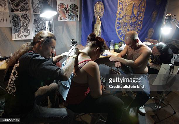 Ein Mann und eine Frau lassen sich in einem Tattoo Studio taetowieren