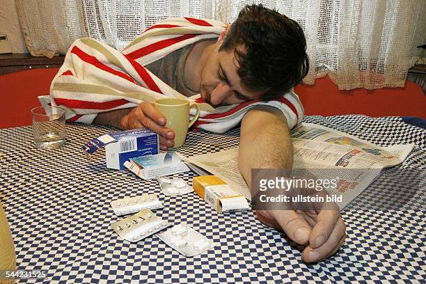 Mann mit Grippe, Erkältung am Küchentisch mit verschiedenen Medikamenten