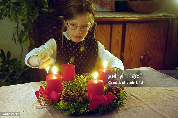Mädchen entzündet eine Kerze auf dem Adventskranz zum dritten Advent- Dezember 2003