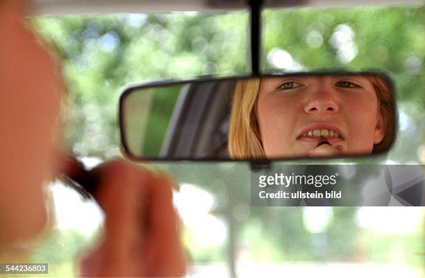 Deutschland, Verkehrssicherheit: Junge Autofahrerin schminkt sich im Rueckspiegel waehrend der Fahrt im Auto