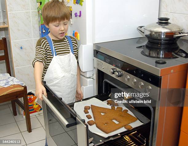 Weihnachtsbäckerei: Kleiner Junge schaut auf sein selbstgebackenes Lebkuchenhaus im Backofen