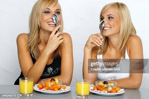 Gesunde Ernaehrung: Blonde Zwillinge mit Obstsalat, Orangensaft und Loeffel