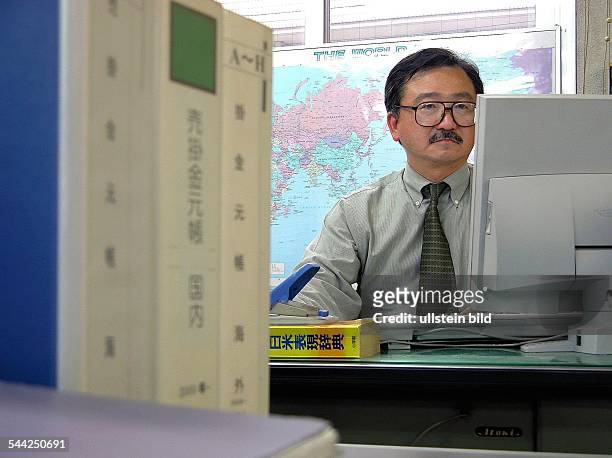 Japanischer Manager an seinem Schreibtisch schaut auf den Computerbildschirm- 2005