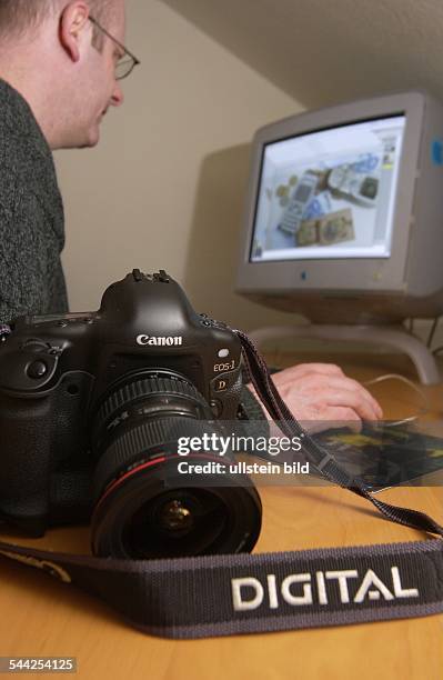 Deutschland, Berlin - Digitale Fotografie, ein Fotograf bearbeitet am Computer seine digitalen Bilddaten, vorne eine Digitalkamera der Firma Canon