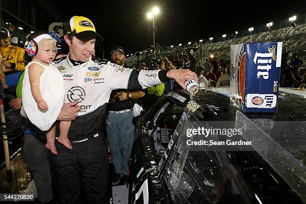 Brad Keselowski, driver of the Detroit Genuine Parts Ford, pours Miller Lite onto his car while holding daughter Scarlett in Victory Lane after...