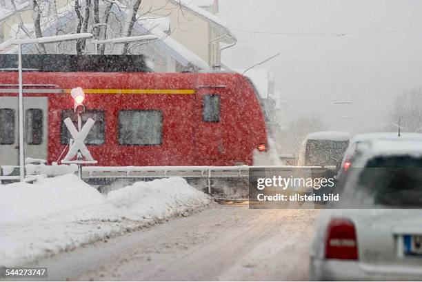 Deutschland , Bayern, Penzberg - Autos warten am am Bahnübergang im Schneegestöber, ein Regionalzug der Deutschen Bahn fährt vorbei