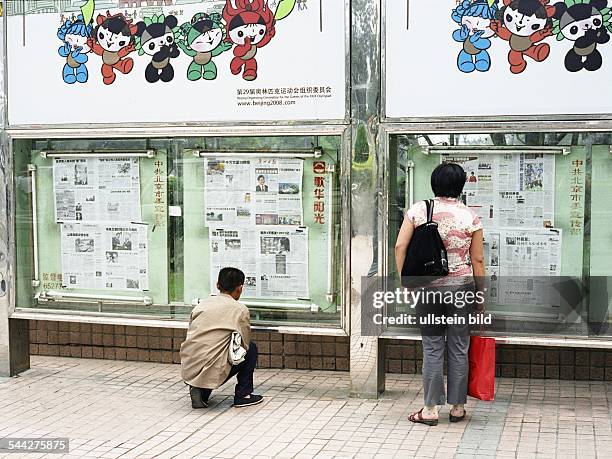 China, Peking : Ein Mann und eine Frau lesen eine in Schaufenstern ausgestellte oeffentliche Zeitung